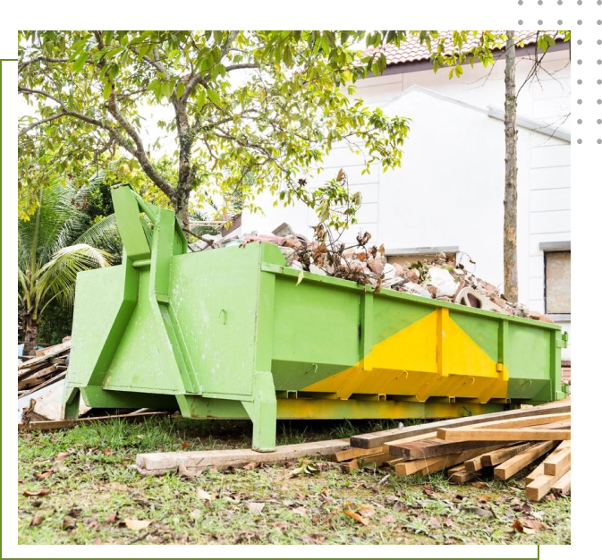 A green and yellow dumpster in the grass.