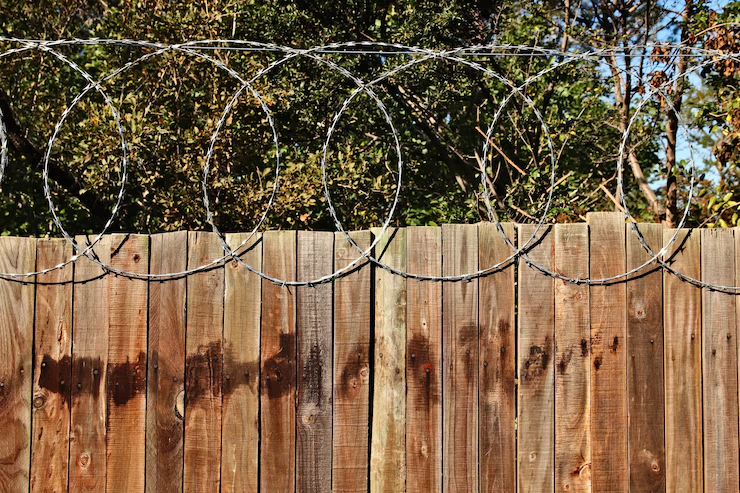 A deteriorating wooden fence with barbed wire and exposed nails in a yard