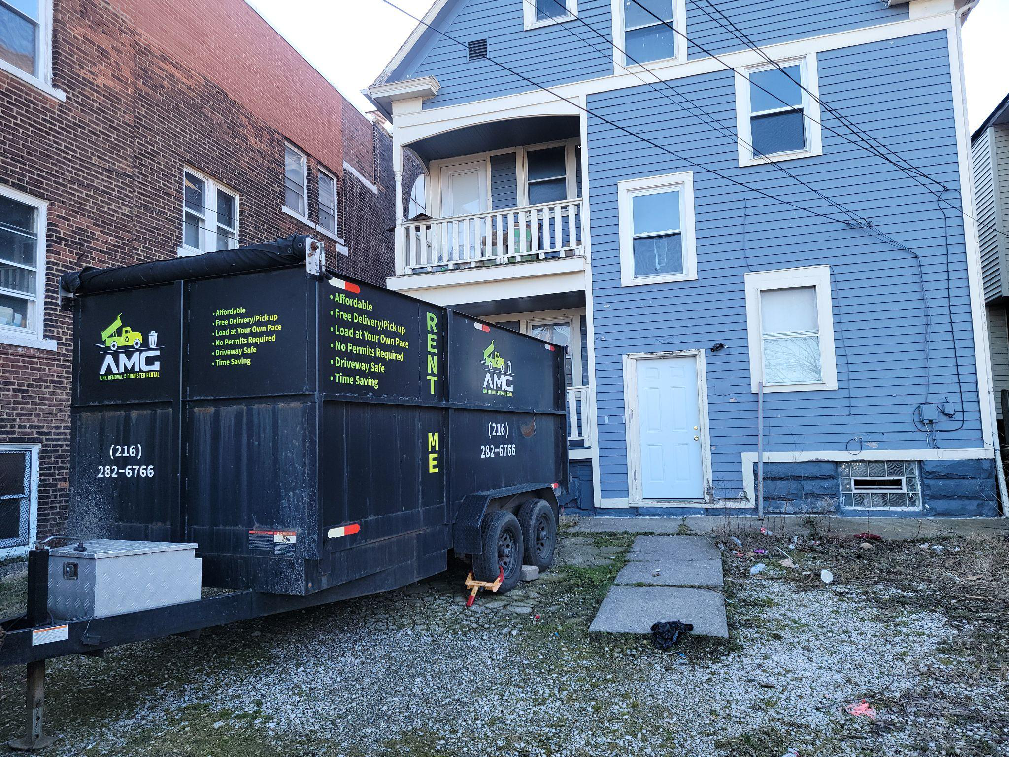 A dumpster parked outside a blue house.
