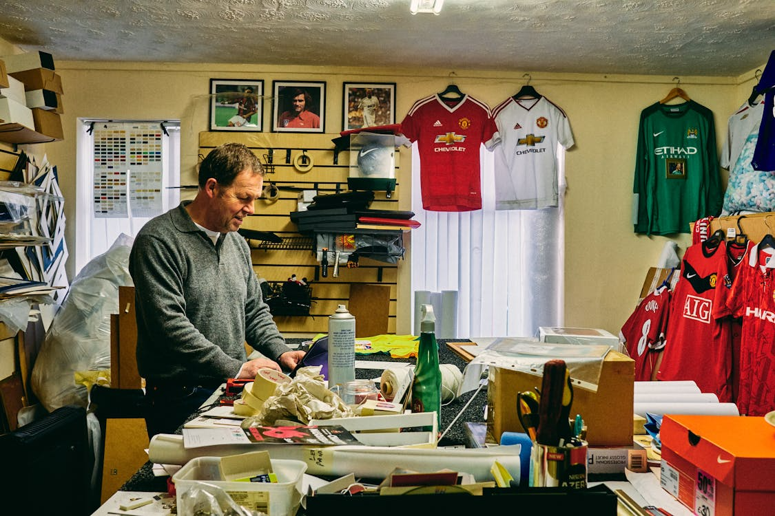 A person working in a football store with cluttered jerseys on the wall.