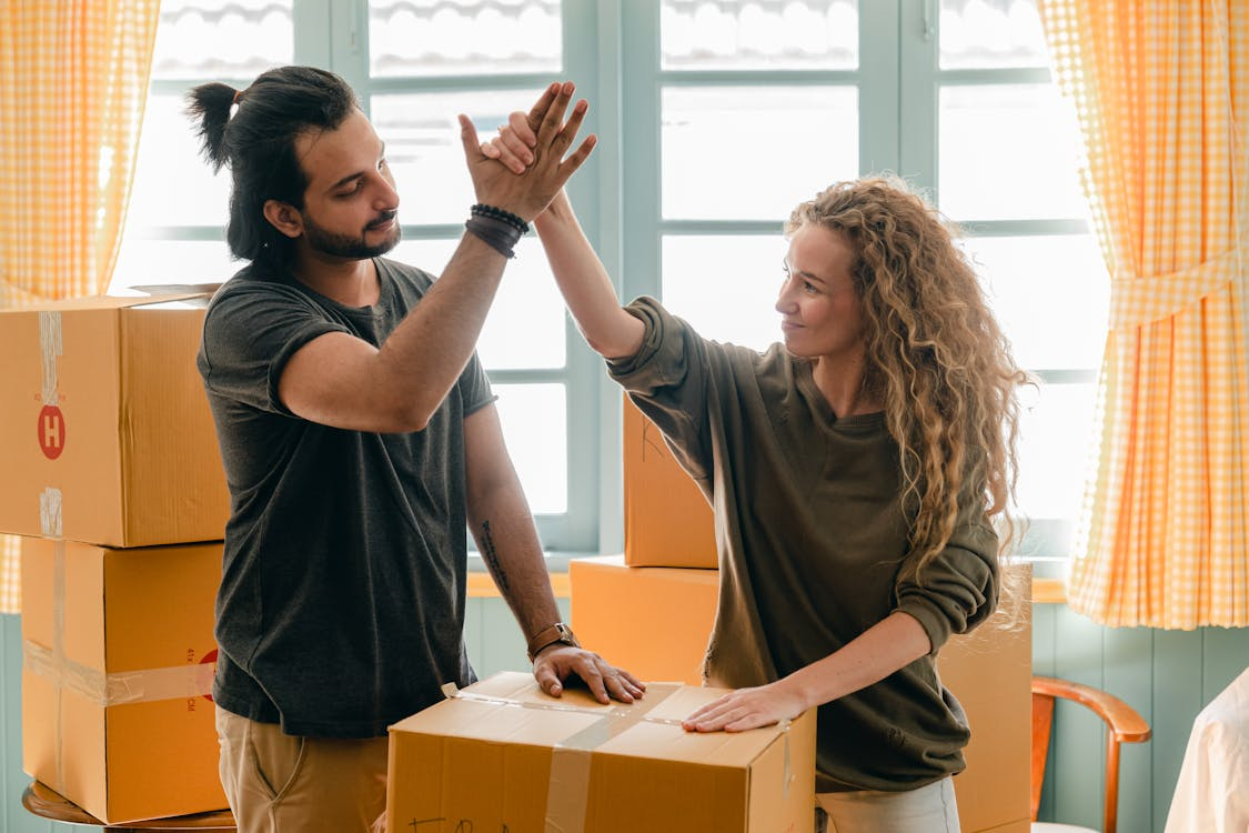 Happy couple high-fiving in a room filled with moving boxes after completing their home cleanout in Bedford.