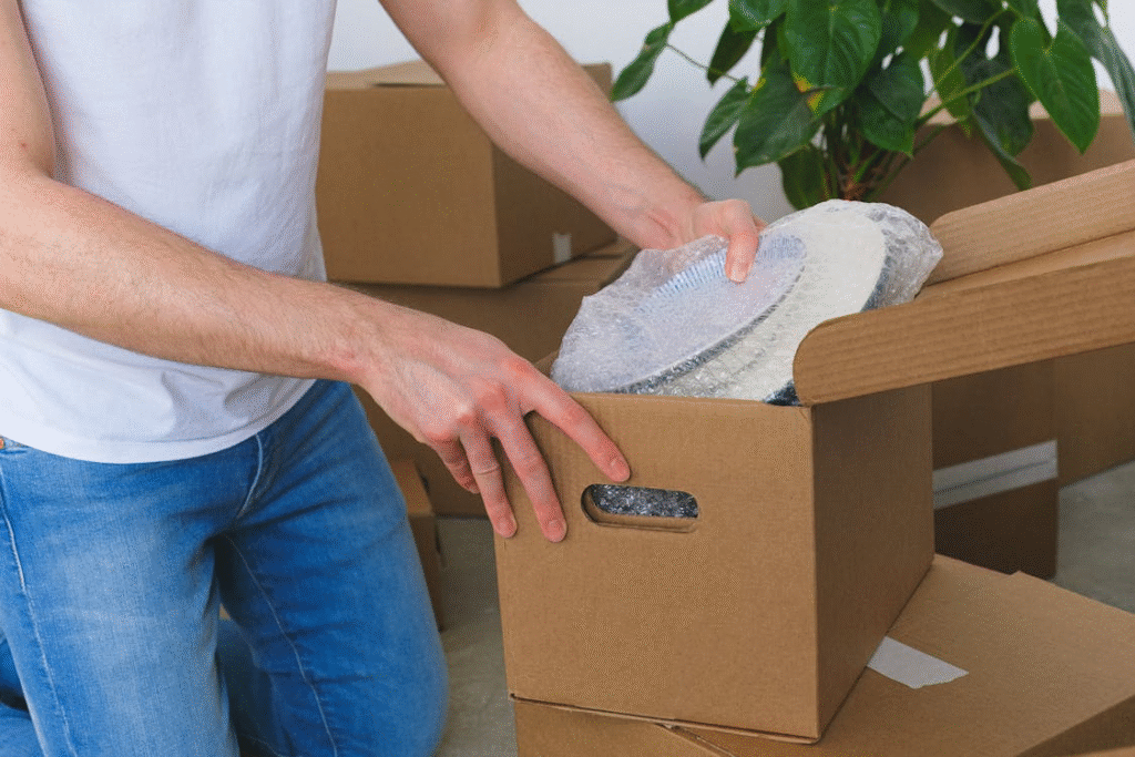 Person packing dishes with bubble wrap into a cardboard box while preparing for a move in Bedford.