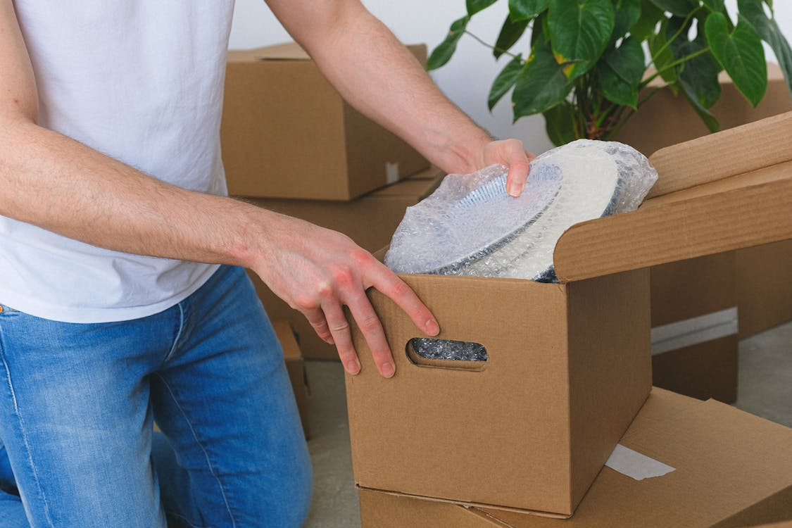 Person packing dishes with bubble wrap into a cardboard box while preparing for a move in Bedford.