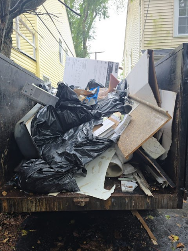 Image of an AMG junk removal truck holding filled trash bags and furniture pieces.